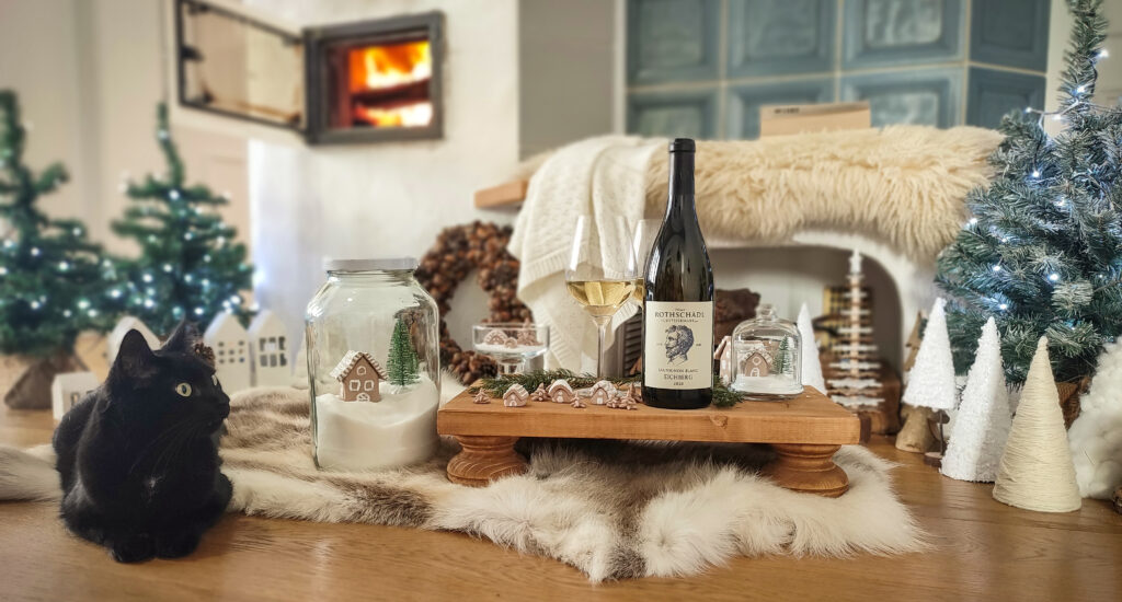 Vor dem Kachelofen ist alles Weihnachtlich geschmückt und eine Flasche wein mit zwei Gläsern stehen bereit. Sammy, die schwarze Katze genießt die Wärme vom Feuer.